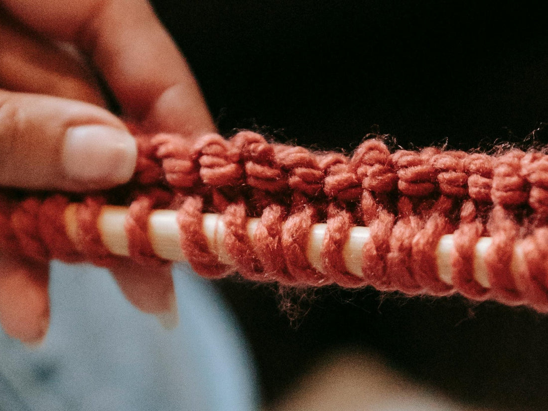 Close-up of hands knitting with red yarn on wooden needles, showing detailed knit stitches