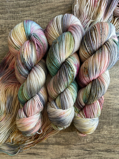 Three skeins of multicolored hand-dyed yarn on wooden surface with soft pastel tones