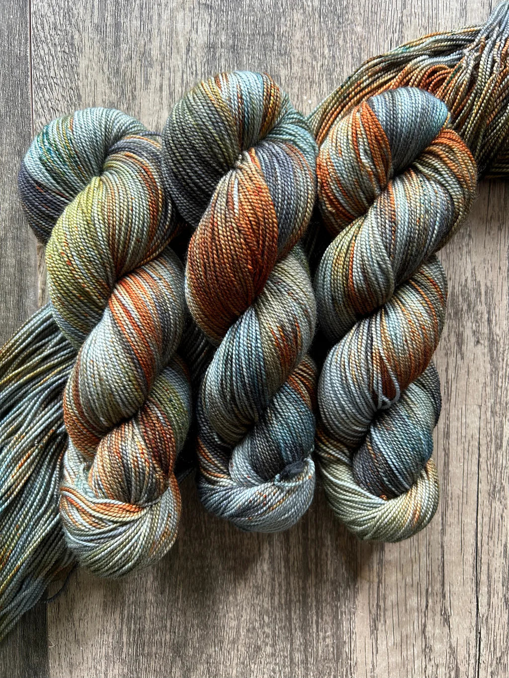 Three skeins of variegated yarn in blue, orange, green, and gray tones on a wooden surface