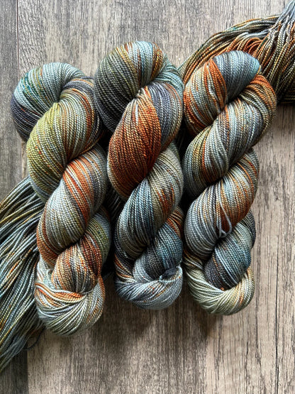 Three skeins of variegated yarn in blue, orange, green, and gray tones on a wooden surface