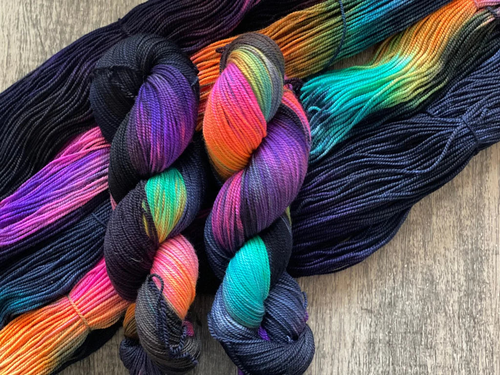 Two skeins of multicolored yarn with vibrant hues of purple, pink, orange, and teal on a wooden surface