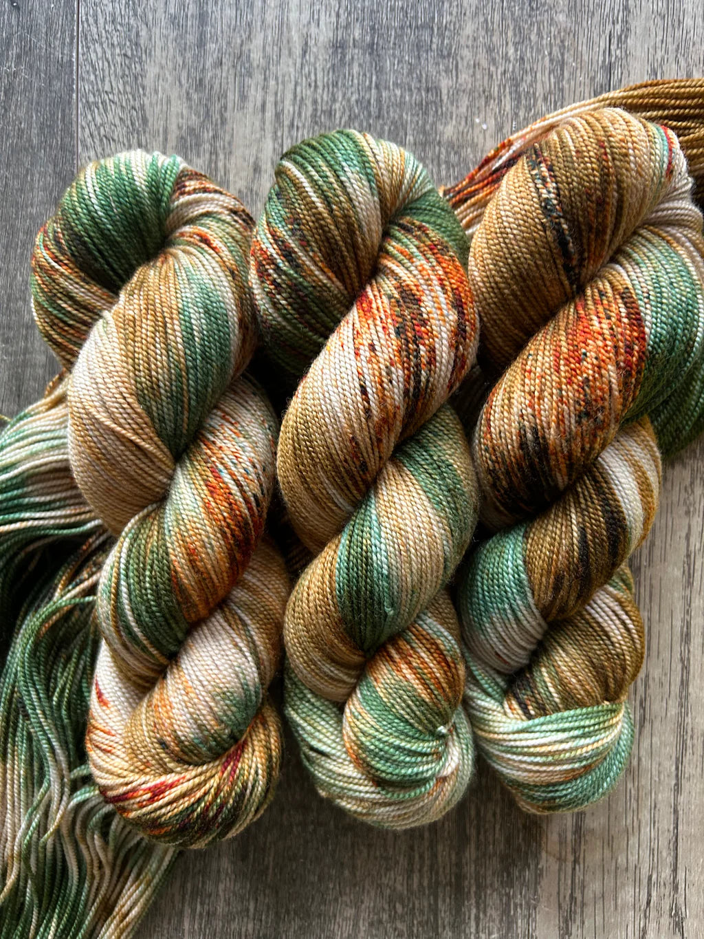 Three skeins of multicolored yarn in green, brown, orange, and cream hues on wooden surface