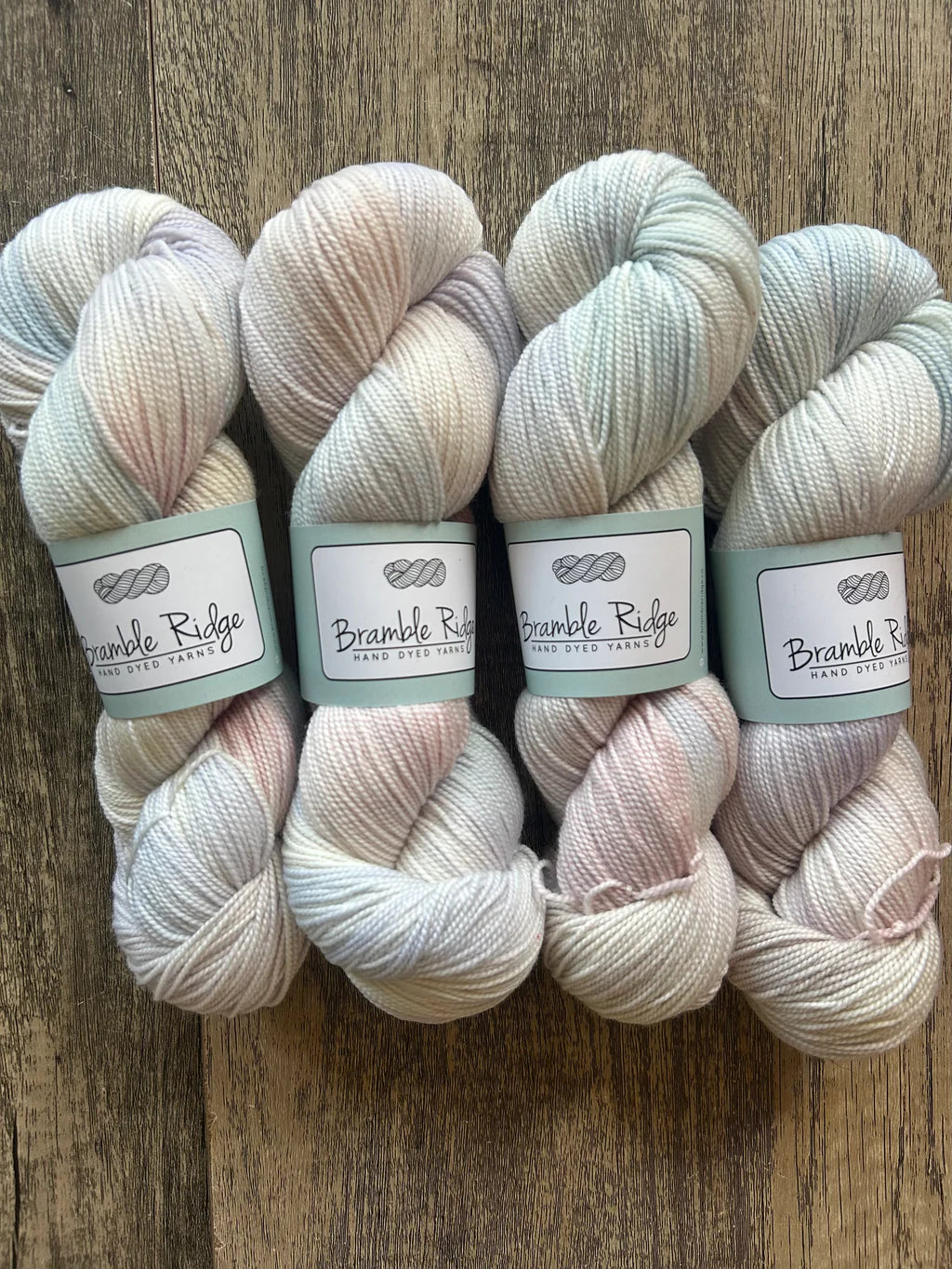 Four skeins of soft pastel hand dyed yarn from Bramble Ridge on wooden surface