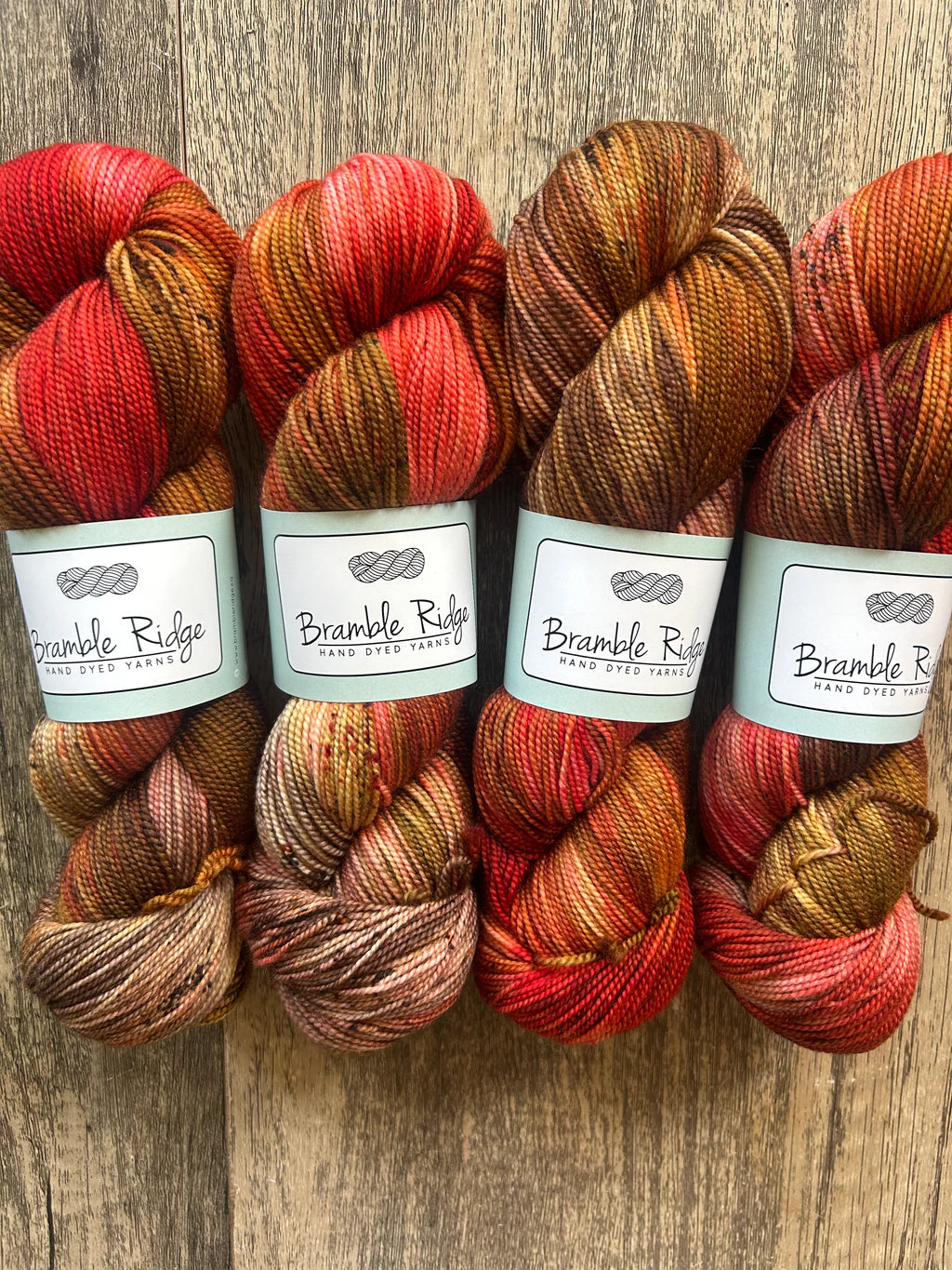 Four skeins of Bramble Ridge hand dyed yarn in warm autumn colors on wooden surface